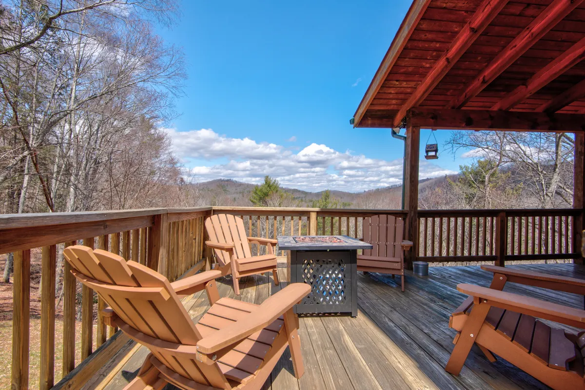 A wooden deck outfitted with Adirondack chairs and a gas fire pit, oriented towards panoramic mountain views. The scene suggests peaceful relaxation and a front-row seat to wildlife and sunsets.