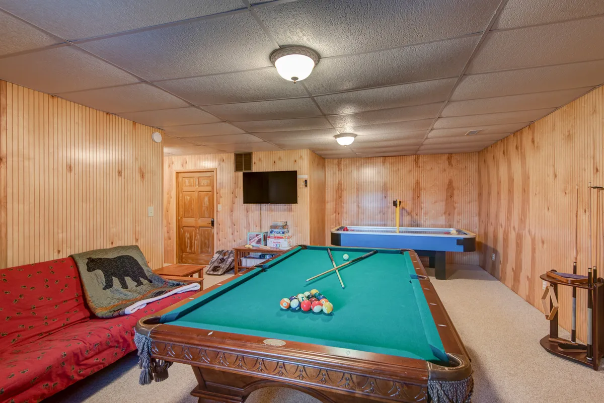 This image showcases a spacious game room featuring a pool table, air hockey table, a comfortable sofa, and a television. The inviting space is designed for group entertainment and lively gatherings, highlighting multiple sources of fun and relaxation.