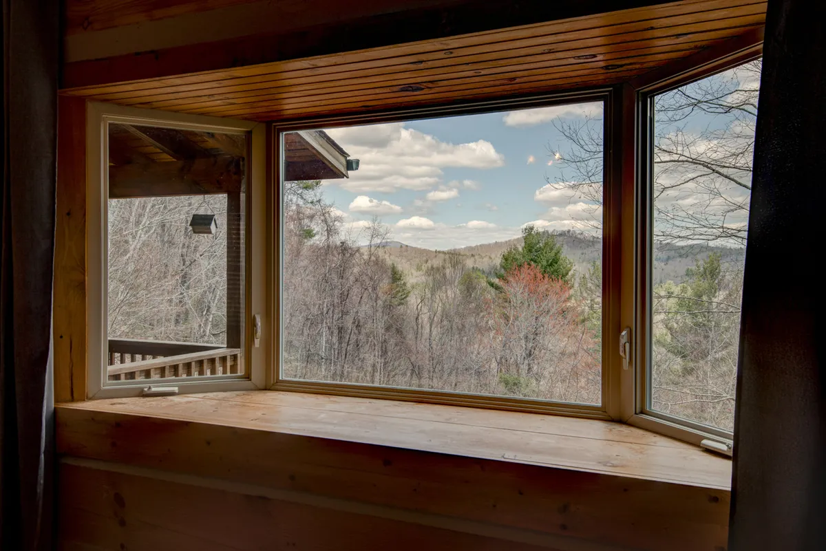 A serene interior shot highlighting a large window framed in wood, with a clear view of the mountain landscape just beyond. The setting invites guests to relax and observe the changing seasons from the comfort of inside.