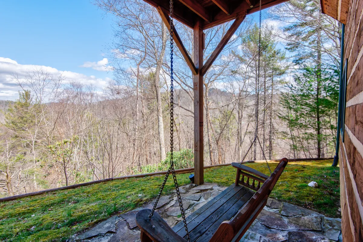 A wooden swing is poised on a deck overlooking a sweeping mountain vista, framed by leafy trees. The sense of peace and connection to the wilderness invites guests to relax, observe wildlife, and take in the scenery after a day of exploration.