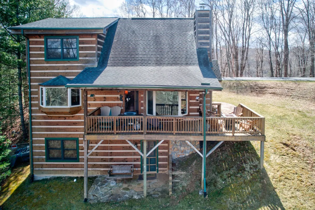 An inviting wooden deck with a sturdy stone foundation and expansive windows looking into the cabin. The deck offers a seamless transition between indoor comforts and the great outdoors, with space for outdoor dining, morning coffee, or simply soaking up the surrounding tranquility. Large windows hint at the open, social interiors described in the section.