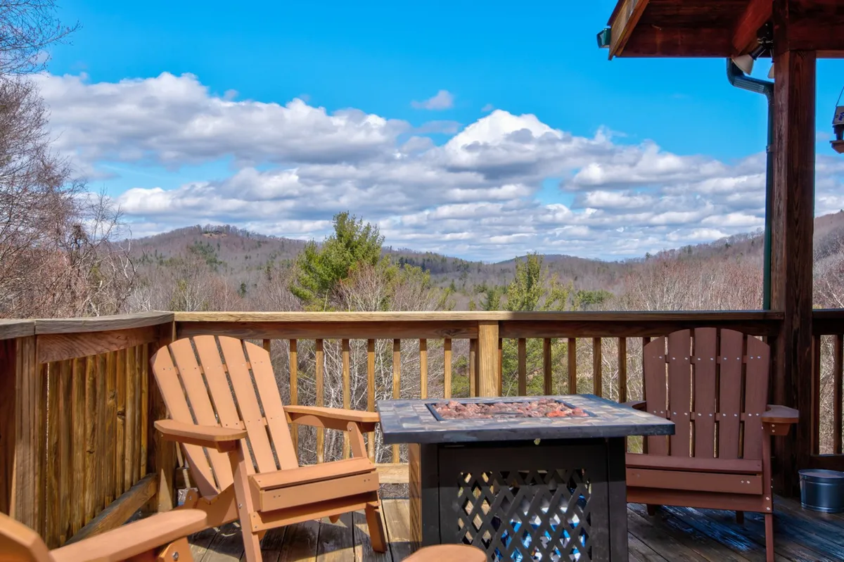 An inviting outdoor stone patio area with Adirondack chairs around a fire pit and a sweeping mountain view. The setting offers a seamless transition from the lively indoor game room to peaceful outdoor relaxation, embodying the 'easy access to the outdoor stone patio' mentioned in the section.
