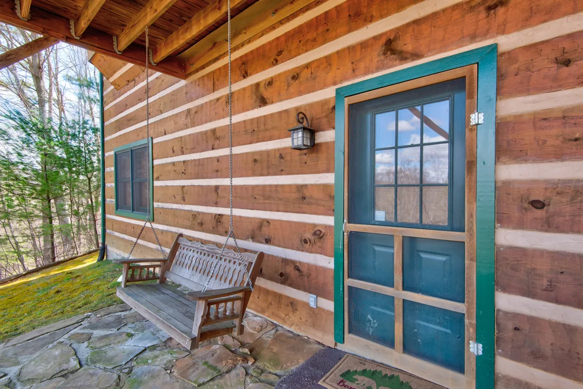 A peaceful exterior scene featuring a wooden swing on the porch, with a view of the natural surroundings. The image captures the tranquility of the area and the comfort of enjoying nature just steps from the cabin door.