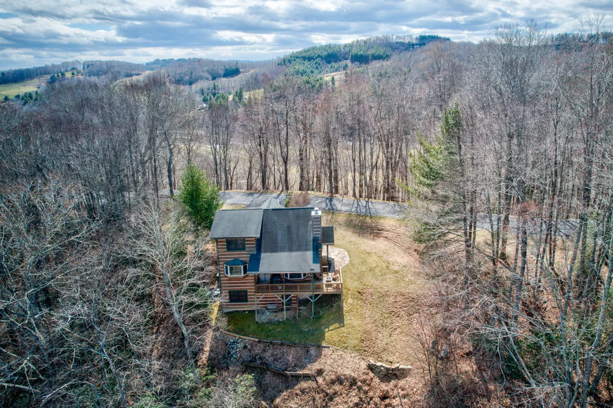 The log cabin stands amidst an open field bordered by trees, with plenty of space for outdoor activities. The broad view showcases the cabin's proximity to nature and the inviting openness of the property.